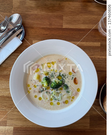 Top view creamy broccoli soup served in white plate on wooden cafe table. Comfort food, healthy lunch concept and modern restaurant dining presentation. Top view creamy broccoli soup served in white plate on wooden cafe table. Comfort food, healthy lunch concept and modern restaurant dining presentation. 137460606