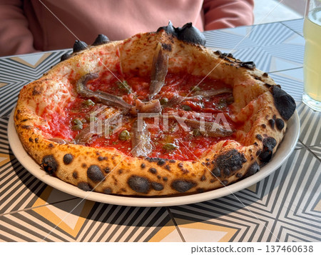 Neapolitan pizza with tomato sauce, anchovy and caper served on a plate in a cafe interior. Italian cuisine, traditional gastronomy, restaurant dining culture and authentic Mediterranean food 137460638