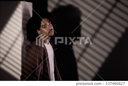 Young african-american man posing near wall with striped shadows Young african-american man posing near wall with striped shadows 137460827