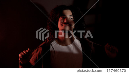 Young latin african-american man with curly hair and goatee is opening his brown hoodie in a dark 137460870