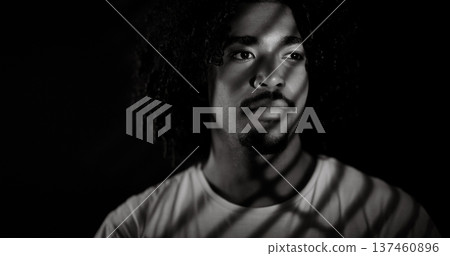 Young african-american man with curly hair looking away with projected shadows on his face Young african-american man with curly hair looking away with projected shadows on his face 137460896