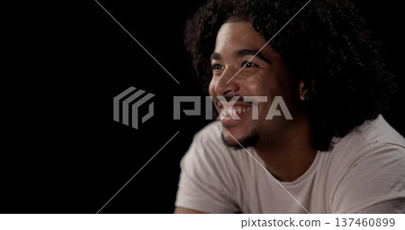 Young african-american man with curly hair smiling and looking away on black background Young african-american man with curly hair smiling and looking away on black background 137460899