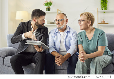 Real estate agent explaining terms to mature couple using tablet in living room Real estate agent explaining terms to mature couple using tablet in living room 137460981