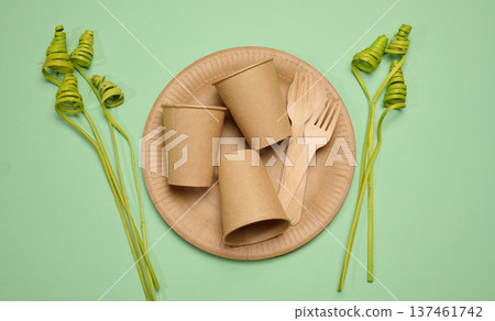 Paper cups and wooden forks on a large craft plate, long green decorative branches Paper cups and wooden forks on a large craft plate, long green decorative branches 137461742