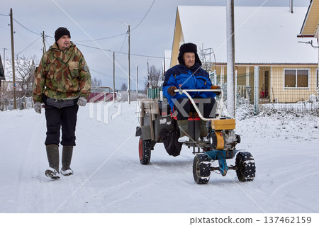 Walk behind tractor used by farmers to transport cargo inside trailer during winter season in rural area. 137462159