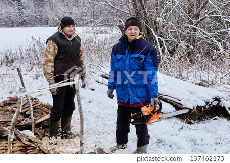 Fuel preparation for wood stoves farmers cut stacked slabwood into pieces using gasoline chainsaw. 137462173
