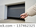 Hand holding remote and keys in front of closed garage door at residential building 137462325