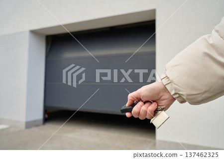 Hand holding remote and keys in front of closed garage door at residential building 137462325
