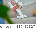 Woman cleaning fabric sofa with handheld vacuum cleaner in living room 137462327