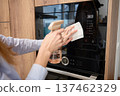 Hands spray and wipe glass door of built in microwave oven in kitchen cabinet 137462329