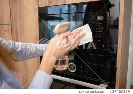Hands spray and wipe glass door of built in microwave oven in kitchen cabinet Hands spray and wipe glass door of built in microwave oven in kitchen cabinet 137462329