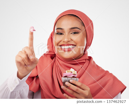 Portrait, cupcake and icing on finger with a muslim woman in studio on a white background for dessert. Face, smile and food with a happy young islamic person eating a cake, candy or sugar snack Portrait, cupcake and icing on finger with a muslim woman in studio on a white background for dessert. Face, smile and food with a happy young islamic person eating a cake, candy or sugar snack 137462927
