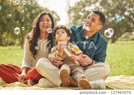 Blowing bubbles, family portrait and happy at park, bonding and having fun together outdoor. Soap toy, child and parents at garden, mother and father smile on picnic blanket, care and play in nature Blowing bubbles, family portrait and happy at park, bonding and having fun together outdoor. Soap toy, child and parents at garden, mother and father smile on picnic blanket, care and play in nature 137463079