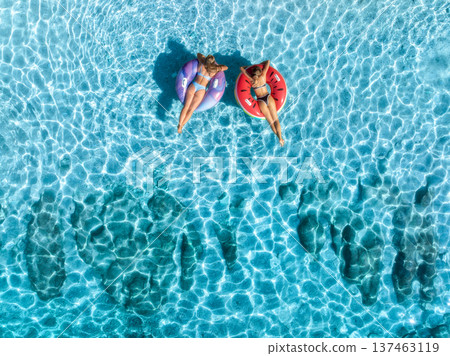 Aerial view of beautiful young women on swim rings in blue sea 137463119