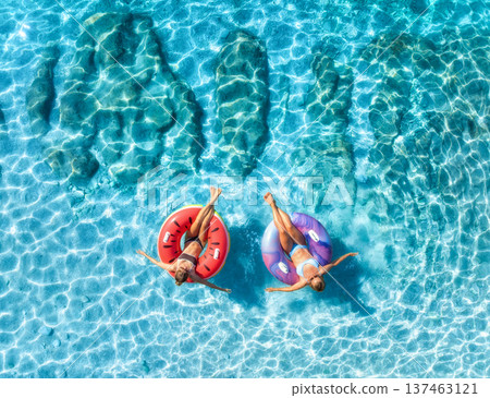 Aerial view of beautiful young women on swim rings in blue sea Aerial view of beautiful young women on swim rings in blue sea 137463121