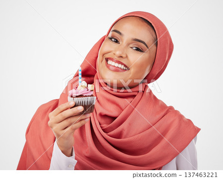 Portrait, candle in a cupcake and an islamic woman in studio on white background for dessert. Face, smile and food with a happy young muslim person eating a cake, candy or sugar snack in celebration Portrait, candle in a cupcake and an islamic woman in studio on white background for dessert. Face, smile and food with a happy young muslim person eating a cake, candy or sugar snack in celebration 137463221