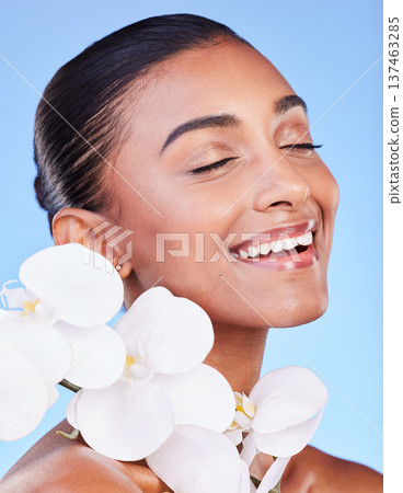 Skincare, flower and happy woman in studio for beauty, wellness and organic body care on blue background. Floral, face and Indian female model smile with orchid for eco friendly dermatology or shine Skincare, flower and happy woman in studio for beauty, wellness and organic body care on blue background. Floral, face and Indian female model smile with orchid for eco friendly dermatology or shine 137463285
