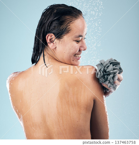 Happy woman, shower and back in water drops with loofah in hygiene, grooming or washing against a blue studio background. Rear view of female person in body wash, cleaning or wet skincare in bathroom 137463758