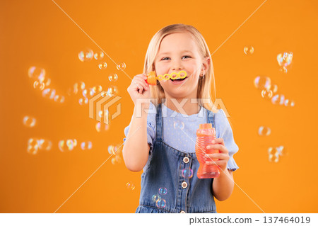 Portrait, happy child and blowing bubbles in studio for fun, freedom and childhood development on orange background. Girl, kid and smile for playing with soap bubble wand, toys and activity games Portrait, happy child and blowing bubbles in studio for fun, freedom and childhood development on orange background. Girl, kid and smile for playing with soap bubble wand, toys and activity games 137464019