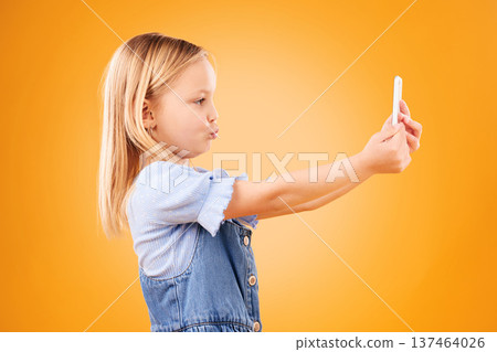 Phone, selfie or profile of kid in studio with confidence or mockup space in photograph memory. Pout, orange background or young girl child taking picture online on a social media app on internet 137464026