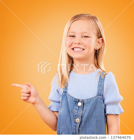 Child, happy portrait and pointing in studio for advertising, announcement or promotion. Excited young girl kid on a orange background for hand gesture, sale or sign for attention or deal offer 137464070