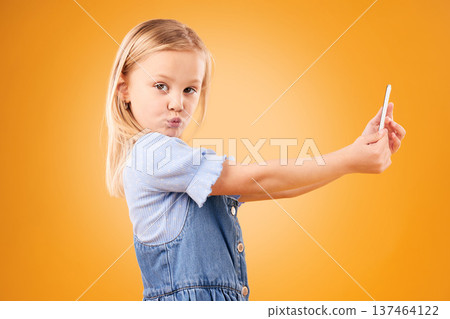 Phone, selfie or portrait of child in studio with confidence or mockup space in photograph memory. Kid, orange background or face of girl taking picture online on a social media app on internet Phone, selfie or portrait of child in studio with confidence or mockup space in photograph memory. Kid, orange background or face of girl taking picture online on a social media app on internet 137464122