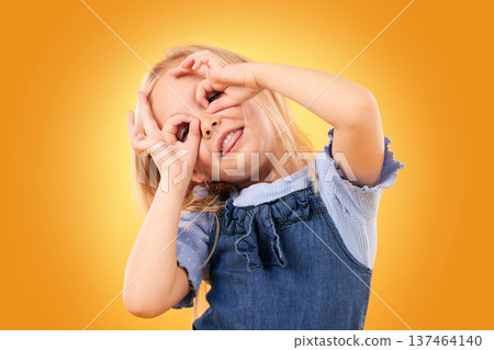 Kids, fun and hand glasses by girl in studio playing, free and funny gesture against orange background space. Finger, frame and child with silly expression, mood or personality, playful or games Kids, fun and hand glasses by girl in studio playing, free and funny gesture against orange background space. Finger, frame and child with silly expression, mood or personality, playful or games 137464140