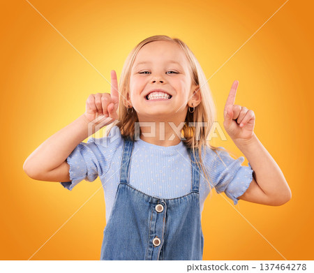 Child, happy portrait and pointing up in studio for advertising, announcement or promotion. Excited young girl kid on a orange background for hand gesture, sale or sign for attention or marketing 137464278