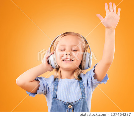 Headphones, happy or child streaming music to relax with freedom in studio on orange background. Hand up, singing or girl singer listening to a radio song, sound or gospel on an online subscription Headphones, happy or child streaming music to relax with freedom in studio on orange background. Hand up, singing or girl singer listening to a radio song, sound or gospel on an online subscription 137464287