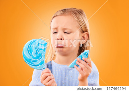 Children, candy and a sad girl with a broken lollipop on an orange background in studio looking upset. Kids, sweets and unhappy with a female child holding a cracked piece of a sugar snack in regret 137464294