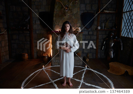 Caucasian woman standing inside pentagram circle, candlelit medieval chamber 137464389