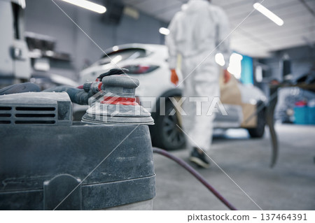 Auto body shop car painting prep with orbital sander and technician in protective suit 137464391
