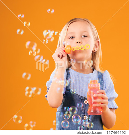 Portrait, child and blowing bubbles in studio for fun, freedom and childhood development on orange background. Young girl, kid and learning to play with soap bubble wand, toys and activity games Portrait, child and blowing bubbles in studio for fun, freedom and childhood development on orange background. Young girl, kid and learning to play with soap bubble wand, toys and activity games 137464392