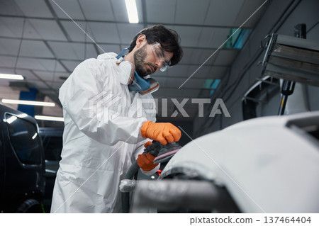 An automotive technician is repairing a car bumper in a workshop while wearing safety gear An automotive technician is repairing a car bumper in a workshop while wearing safety gear 137464404