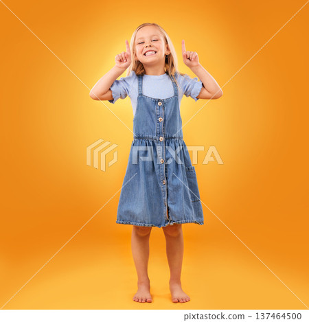 Happy, child portrait and pointing up in studio for advertising, announcement or promotion. Excited barefoot girl kid on orange background for hand gesture, sale or sign for attention or mockup space 137464500