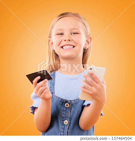 Portrait, child and credit card with phone in studio for online shopping order, digital payment and fintech on orange background. Happy girl kid, smartphone and buy mobile games, sales and savings Portrait, child and credit card with phone in studio for online shopping order, digital payment and fintech on orange background. Happy girl kid, smartphone and buy mobile games, sales and savings 137464504