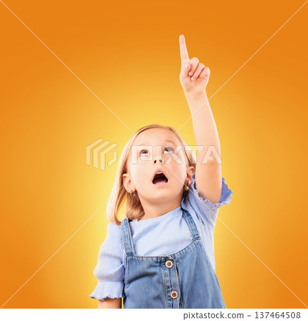 Child, surprise and pointing up with hand in studio for advertising, announcement or promotion. Shocked girl kid on a orange background for gesture, mockup space or sign for attention, fear or scared 137464508
