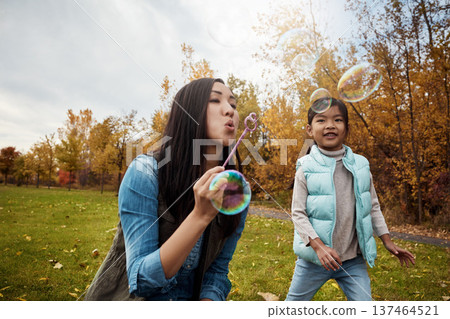 Asian, daughter and mother blowing with bubbles in park for playful childhood or outdoor bonding. Mom, kid or child with wand for parenting, development or fun magical moments together in nature 137464521