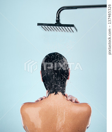 Woman, shower and back in water drops for washing, grooming or hygiene against a blue studio background. Rear view of female person in body wash, cleaning or skincare routine under rain in bathroom 137465326