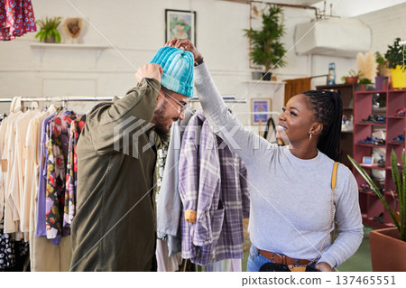 Man, woman and shopping for beanie, store and smile with discount, sale and deal with fitting for fashion. Young couple, thinking and choice with clothes, style and happy with helping hand in mall Man, woman and shopping for beanie, store and smile with discount, sale and deal with fitting for fashion. Young couple, thinking and choice with clothes, style and happy with helping hand in mall 137465551