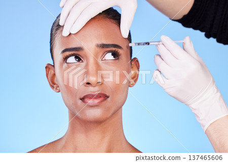 Injection, hands and face of Indian woman for plastic surgery, cosmetics and skincare in studio. Dermatology needle, anxiety and surgeon and person for anti aging, derma and beauty on blue background Injection, hands and face of Indian woman for plastic surgery, cosmetics and skincare in studio. Dermatology needle, anxiety and surgeon and person for anti aging, derma and beauty on blue background 137465606