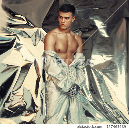 Fashion, sci fi and silver with a trendy man at a photo shoot in a shiny outfit for futuristic style. Cyberpunk, creative or artistic with a young model in studio for holographic or vaporwave clothes 137465689
