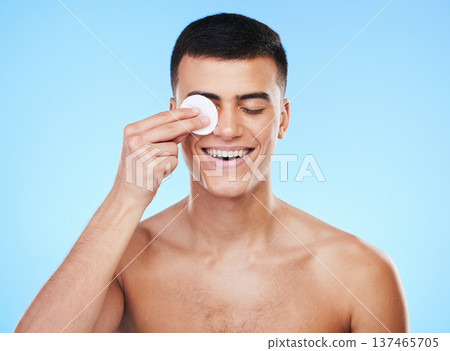 Skincare, beauty and man with cotton pad in a studio for health, wellness and self care routine. Smile, dermatology and young male model cleaning with facial cosmetic swab product on blue background Skincare, beauty and man with cotton pad in a studio for health, wellness and self care routine. Smile, dermatology and young male model cleaning with facial cosmetic swab product on blue background 137465705