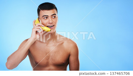 Phone call, banana and young man in a studio for conversation, gossip or funny discussion. Happy, communication and male model from Canada with fruit cellphone by blue background with mockup space. 137465706