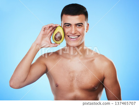 Avocado, wellness and portrait with skincare and natural facial treatment in studio. Blue background, health food and cosmetics with male model holding fruit for nutrition for face and beauty glow Avocado, wellness and portrait with skincare and natural facial treatment in studio. Blue background, health food and cosmetics with male model holding fruit for nutrition for face and beauty glow 137465707