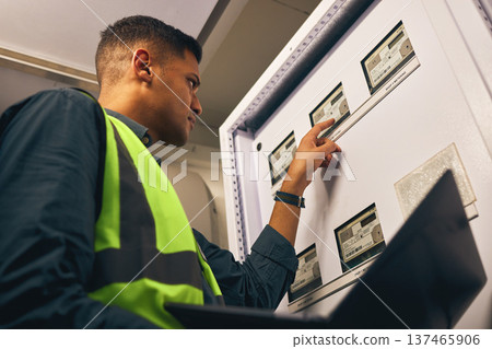 Man, maintenance and control room with laptop, electrician with inspection and fixing electricity supply. Check power grid, pc software and engineering, fuse box and technician with quality assurance 137465906