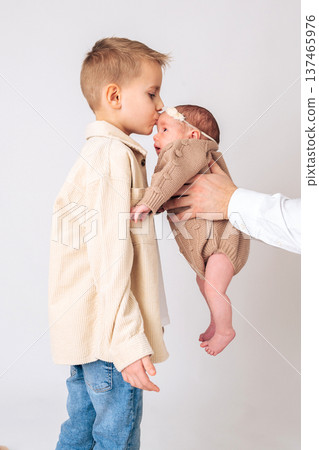 Young boy gently kissing a newborn baby while an adult holds the infant. Tender moment between siblings showing family love, care and protection. Concept of brotherhood, childhood bonding and happy 137465976