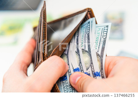 Man placing dollar banknotes into leather wallet. Cash payment, salary income, savings and financial planning concept. 137466255