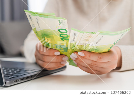 Woman counting euro banknotes while typing notes on laptop. Personal finance, budgeting, online accounting, small business management and money planning concept. Woman counting euro banknotes while typing notes on laptop. Personal finance, budgeting, online accounting, small business management and money planning concept. 137466263