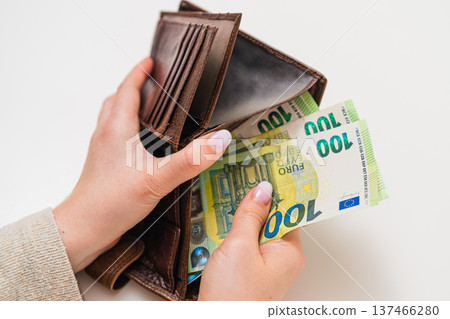 Close view of female hands inserting 100 euro bills into leather wallet. Savings, investment, banking, financial independence, European currency and economic stability theme. 137466280
